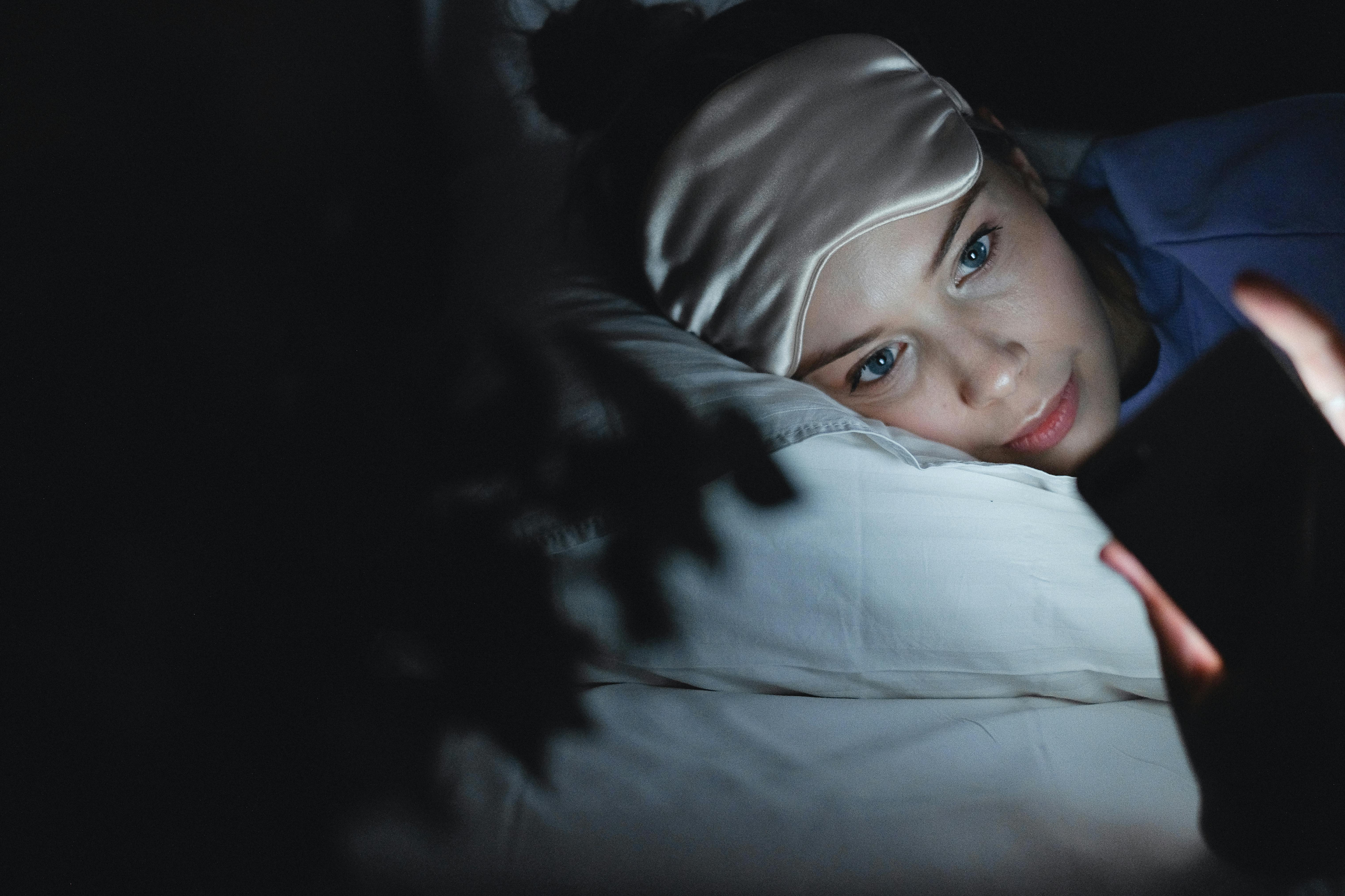 Person in bed at night looking tired while using their phone, symbolizing constant DM monitoring for bookings.